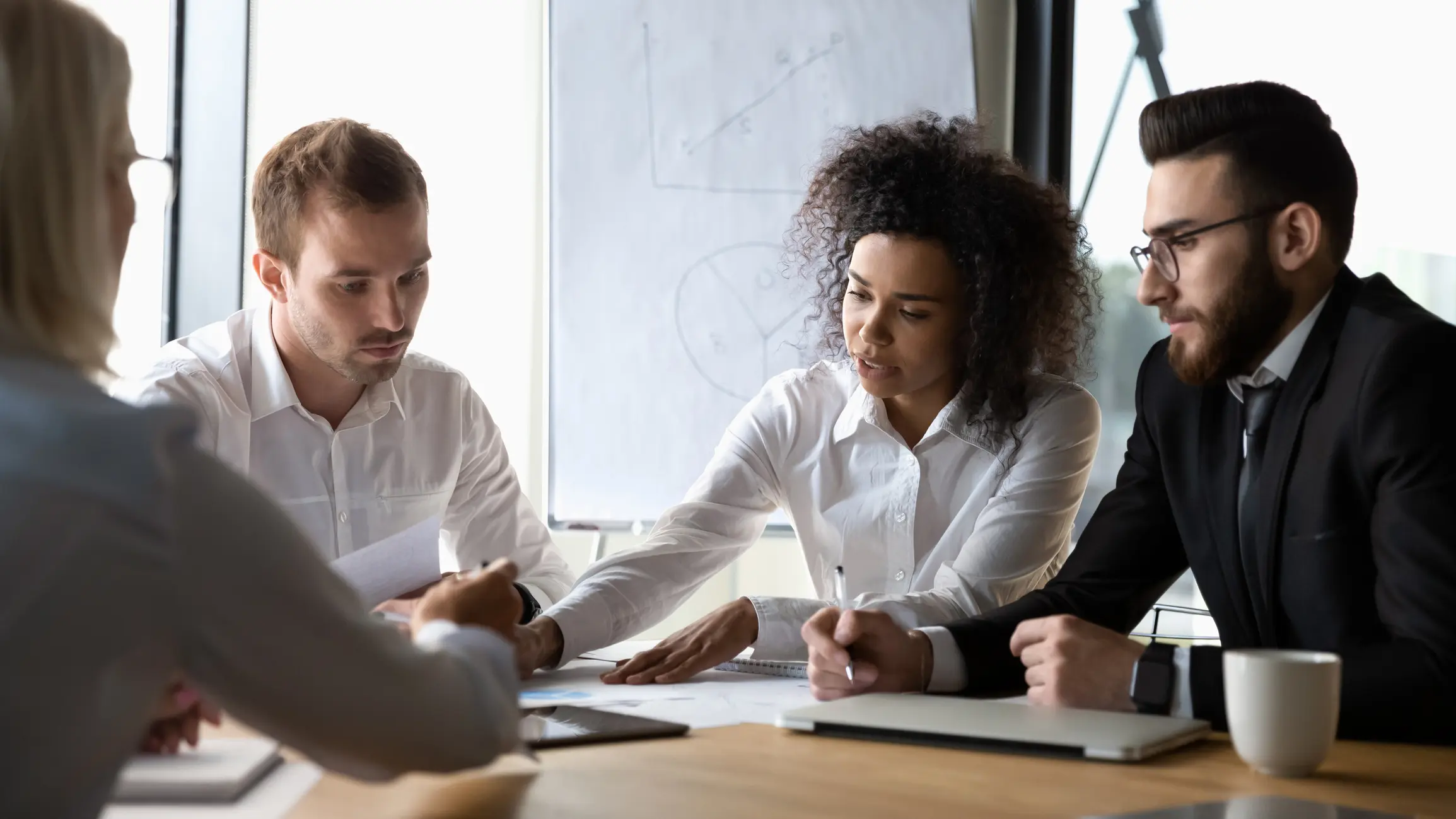 Focused diverse corporate business team participating at group brainstorming financial report discussion, analyzing paperwork, engaged in teamwork at office meeting lead by african woman company boss